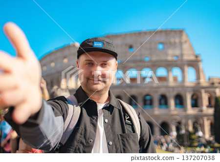 Handsome 30s tourist visiting Colosseum in Rome, Italy. Young man taking photo in front of famous Italian landmark  137207038