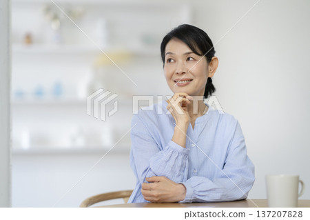 A woman in her late 50s sitting at a dining table and smiling 137207828