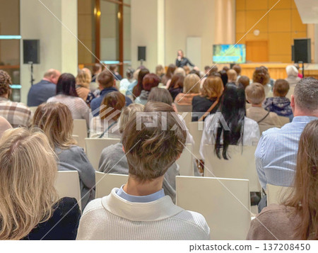 Audience seated in hall listening to speaker, business conference with screen. Education Workshop Session. Forum Presentation. Professional Networking Meeting. Corporate Training Seminar, training 137208450