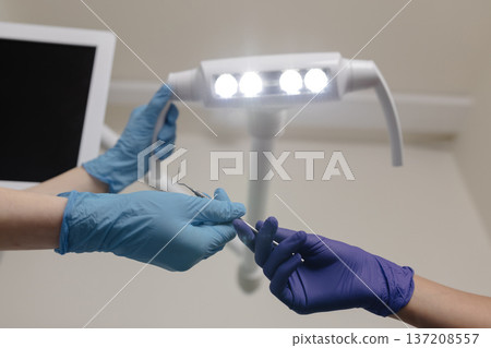 Dentist adjusts lamp before seeing patient, assistant gives instruments 137208557