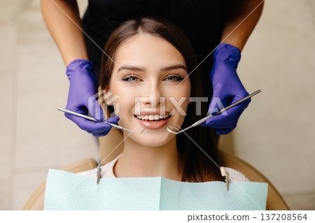Happy patient during a visit to the dentist. The doctor is checking teeth using a dental instrument, ensuring proper oral care in the dentistry clinic Happy patient during a visit to the dentist. The doctor is checking teeth using a dental instrument, ensuring proper oral care in the dentistry clinic 137208564