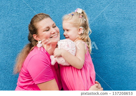 Deaf child with cochlear implant for hearing audio and aid for impairment having fun and laughs with mother outdoor in summer. Sound fitting device to help with communication listening and interaction 137208653