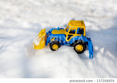 Colorful toy tractor with front loader parked on white snow in bright winter sunlight Colorful toy tractor with front loader parked on white snow in bright winter sunlight 137208859