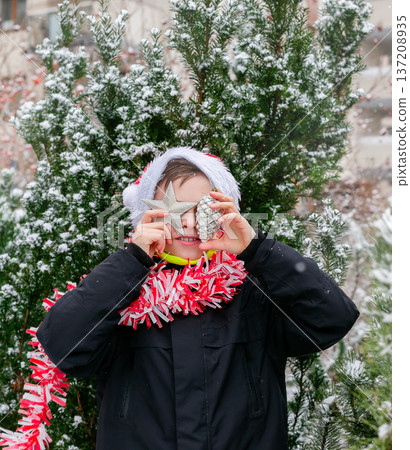 Child dressed as Santa with white beard with Christmas tree decorations in snowy winter garden Child dressed as Santa with white beard with Christmas tree decorations in snowy winter garden 137208935