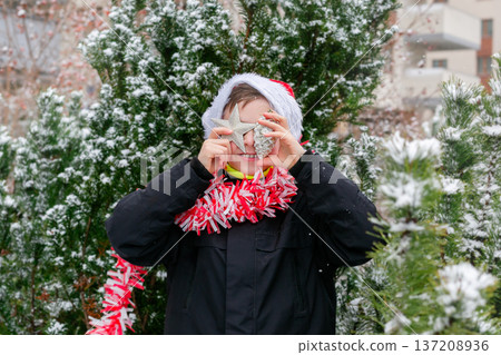 Child dressed as Santa with white beard with Christmas tree decorations in snowy winter garden Child dressed as Santa with white beard with Christmas tree decorations in snowy winter garden 137208936