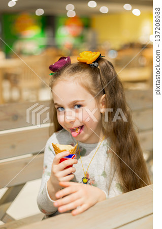 Smiling little girl holding ice cream cone while sitting wooden table cozy cafe with warm lighting 137208988