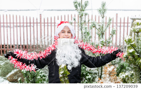 Child dressed as Santa with white beard with Christmas tree decorations in snowy winter garden 137209039
