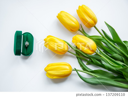 Green velvet ring box with diamond engagement ring beside yellow tulips light background romantic Green velvet ring box with diamond engagement ring beside yellow tulips light background romantic 137209110
