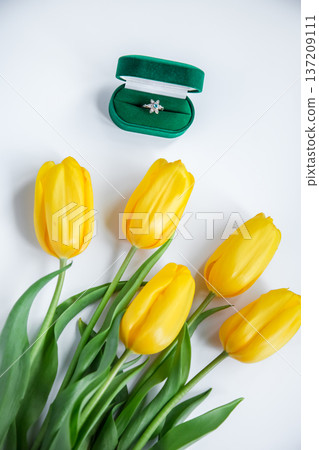 Green velvet ring box with diamond engagement ring beside yellow tulips light background romantic Green velvet ring box with diamond engagement ring beside yellow tulips light background romantic 137209111