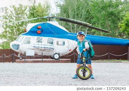 Little boy riding balance bike in front of blue helicopter displayed outdoors in city park area Little boy riding balance bike in front of blue helicopter displayed outdoors in city park area 137209243