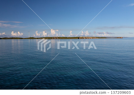 沖繩平靜的海面,遠處島嶼上的風力發電設施。 沖繩平靜的海面,遠處島嶼上的風力發電設施。 137209603