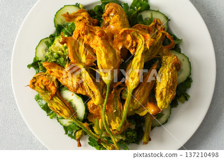 Roasted zucchini flowers sit on a bed of salad made with fresh greens, cucumbers, and broccoli. This dish highlights summer flavors and healthy eating options Roasted zucchini flowers sit on a bed of salad made with fresh greens, cucumbers, and broccoli. This dish highlights summer flavors and healthy eating options 137210498