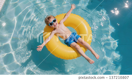 Happy boy in sunglasses floating on yellow inflatable ring in clear swimming pool water on sunny summer day 137210807