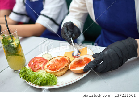 Chef spreads sauce on burger buns with spoon Chef spreads sauce on burger buns with spoon 137211501
