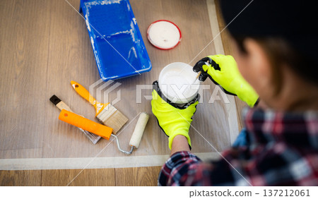 Female Worker mixes white paint in a bucket while preparing to paint a Walls in Room Female Worker mixes white paint in a bucket while preparing to paint a Walls in Room 137212061