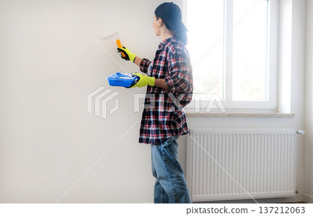 Woman painting walls with a roller and White Paint During Painting Renovation Rooms 137212063