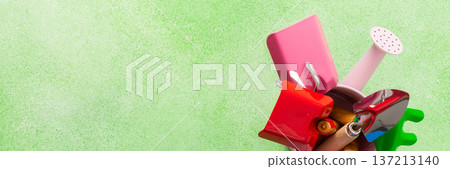 Colorful gardening tools arranged in a small bucket on a green surface ready for spring planting, banner 137213140