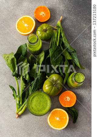 Juice is being made from fresh greens like spinach, chard, and broccoli along with oranges and tangerines. The process takes place in summer with bright colors and natural ingredients 137213180