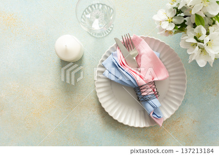 A beautiful spring table setting showcases soft pastel napkins neatly arranged on a plate alongside a candle and fresh flowers, creating an inviting dining atmosphere 137213184