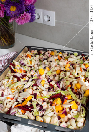 Fresh vegetables are chopped and placed on a baking tray ready for cooking in the oven. Colorful ingredients are showcased, and the setting is a welcoming kitchen 137213185