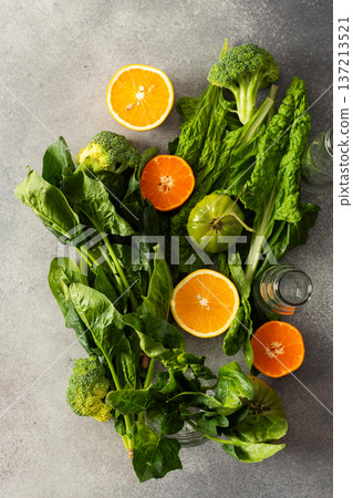Fresh spinach, chard, and broccoli sit among sliced oranges and tangerines as juice is prepared in a kitchen. The scene captures a vibrant approach to healthy drinking Fresh spinach, chard, and broccoli sit among sliced oranges and tangerines as juice is prepared in a kitchen. The scene captures a vibrant approach to healthy drinking 137213521