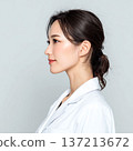 A young woman wearing a white coat looking sideways 137213672