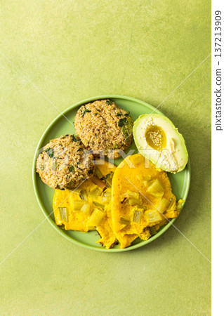 A colorful breakfast spread featuring scrambled eggs mixed with rhubarb, quinoa pancakes, and sliced avocado drizzled with olive oil, all served on a green plate A colorful breakfast spread featuring scrambled eggs mixed with rhubarb, quinoa pancakes, and sliced avocado drizzled with olive oil, all served on a green plate 137213909