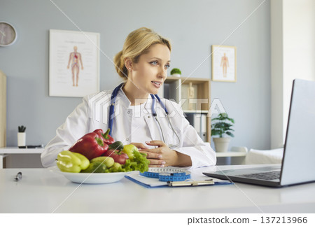 Dietitian with fresh vegetables near conducts telehealth consultation via laptop Dietitian with fresh vegetables near conducts telehealth consultation via laptop 137213966