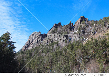 Towering rock formations of Krasnoyarsk Stolby national park in winter with mixed forest under a clear blue sky. Nature reserve landscape. Takmak rock Towering rock formations of Krasnoyarsk Stolby national park in winter with mixed forest under a clear blue sky. Nature reserve landscape. Takmak rock 137214063