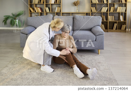Nurse assisting elderly woman with knee pain after home fall, caregiving aid 137214064