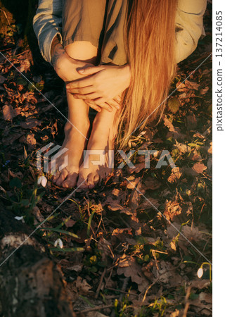 Woman Sitting Barefoot in Forest with Snowdrops Flowers 137214085