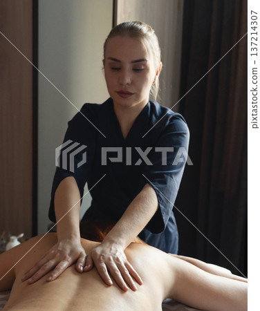 Therapist hands performing a deep tissue massage on a woman's back, promoting relaxation and wellness in a calm spa setting 137214307