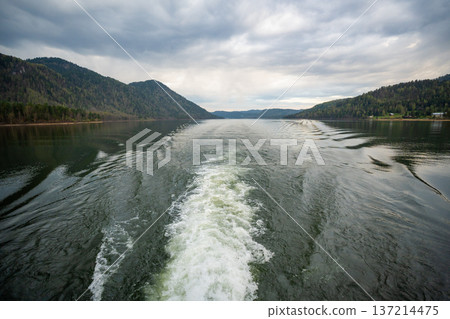 Wake trail behind ferry moving across Teletskoye lake in Altai Russia. Tranquil water surface with distant shoreline and mountains 137214475