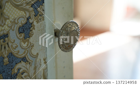 Decorative metal door knob on patterned vintage wallpaper in softly lit interior Decorative metal door knob on patterned vintage wallpaper in softly lit interior 137214958