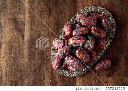Dried dates fruit in silver tray on a wooden table. Dried dates fruit in silver tray on a wooden table. 137215225