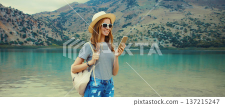 Summer vacation, happy young woman tourist using mobile phone on lake and mountains background Summer vacation, happy young woman tourist using mobile phone on lake and mountains background 137215247