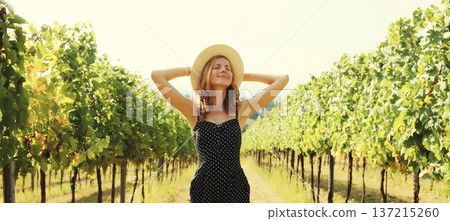 Happy young woman tourist in a summer hat enjoying sunny view of a vineyard in Italy Happy young woman tourist in a summer hat enjoying sunny view of a vineyard in Italy 137215260