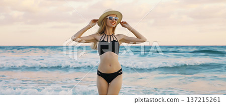 Summer vacation, beautiful happy slim woman in black swimsuit, tourist hat on the beach on sea Summer vacation, beautiful happy slim woman in black swimsuit, tourist hat on the beach on sea 137215261