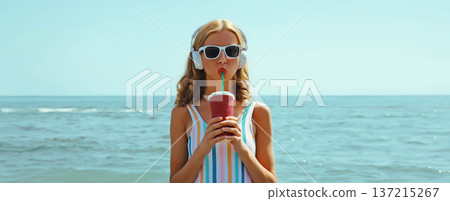 Summer portrait happy relaxed young woman enjoys listening to music with headphones on beach at sea Summer portrait happy relaxed young woman enjoys listening to music with headphones on beach at sea 137215267