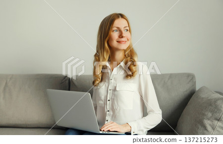 Happy modern woman working with laptop, freelancer girl sitting on a couch in the living room Happy modern woman working with laptop, freelancer girl sitting on a couch in the living room 137215273