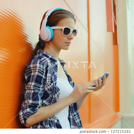 Modern young woman listening to music with smartphone, girl in headphones holding phone Modern young woman listening to music with smartphone, girl in headphones holding phone 137215281
