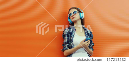 Modern young woman listening to music with smartphone, girl in headphones holding phone 137215282