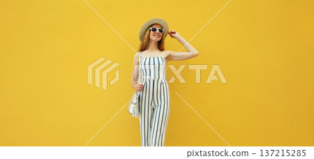 Summer outfit, stylish beautiful young woman posing in white striped jumpsuit against yellow wall Summer outfit, stylish beautiful young woman posing in white striped jumpsuit against yellow wall 137215285