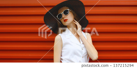 Beautiful stylish young woman in summer black hat, fashionable girl model standing on red background Beautiful stylish young woman in summer black hat, fashionable girl model standing on red background 137215294