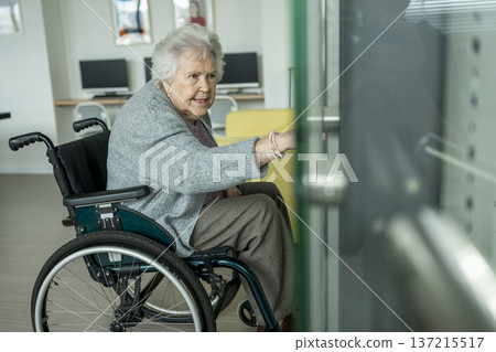 Senior woman in wheelchair entering glass elevator. Senior woman in wheelchair entering glass elevator. 137215517