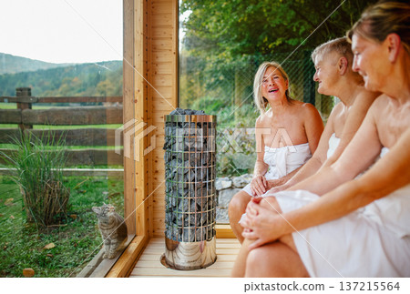 Senior women relaxing together in wooden sauna cabin with countryside view. Senior women relaxing together in wooden sauna cabin with countryside view. 137215564