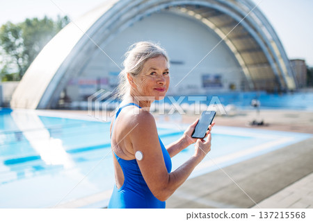 Diabetic senior woman checking glucose on her phone before swimming. 137215568