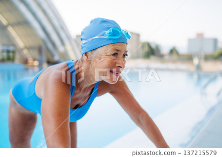 Older female swimmer stretching before swim in pool. Older female swimmer stretching before swim in pool. 137215579