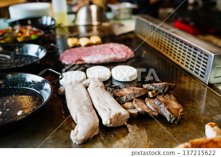Grilled meat and vegetables on teppanyaki grill in restaurant kitchen. Grilled meat and vegetables on teppanyaki grill in restaurant kitchen. 137215622