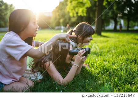 Young girl students learning about nature and wildlife in urban environment, using binoculars and observing animals in public park. 137215647